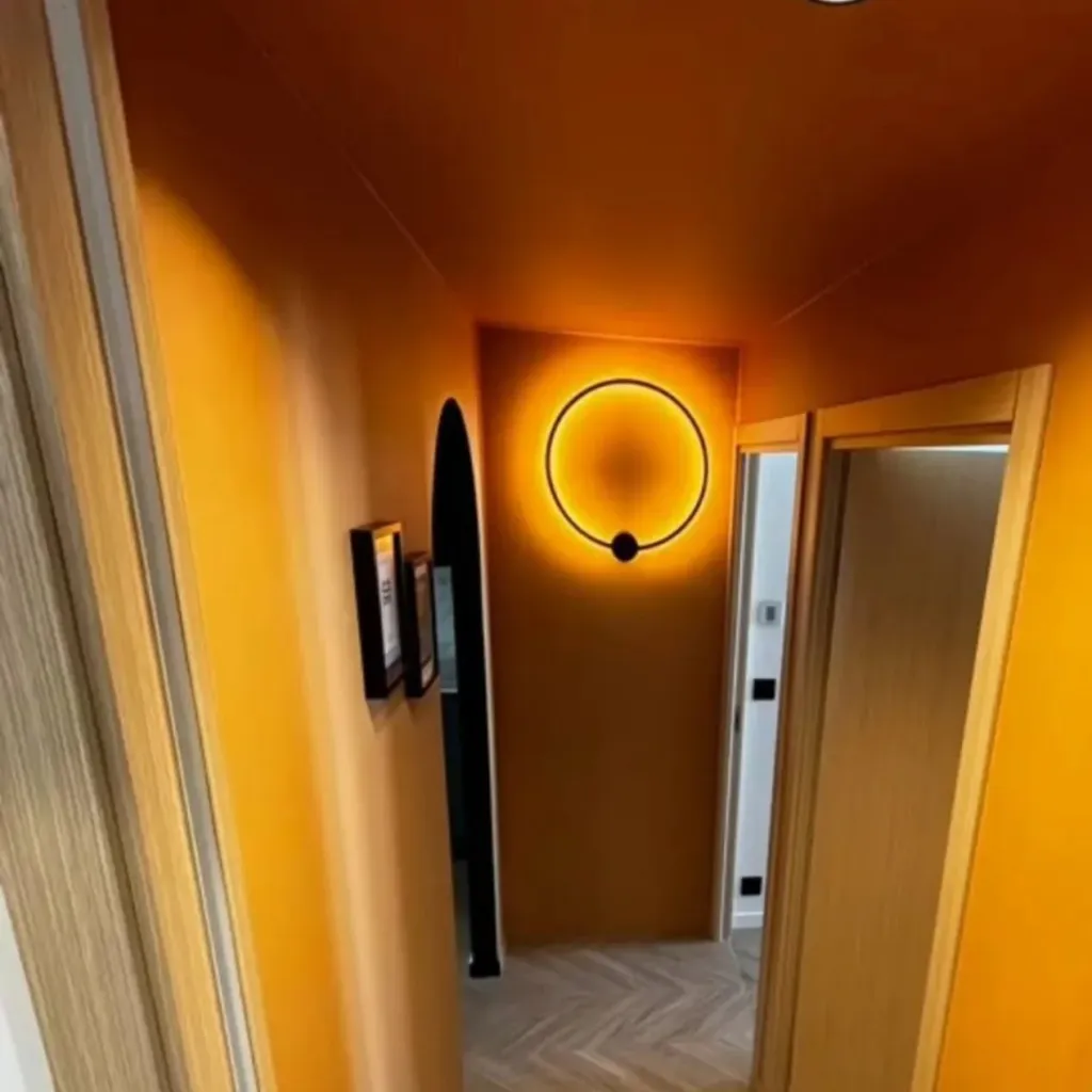 Couloir peint en ambre avec applique lumineuse en anneau, porte en chêne et parquet à chevrons.
