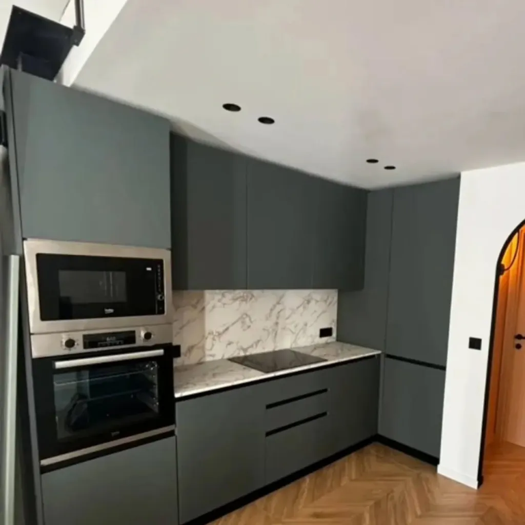 Cuisine linéaire vert sauge avec four et micro-ondes encastrés, plan de travail et crédence effet marbre, parquet à chevrons.