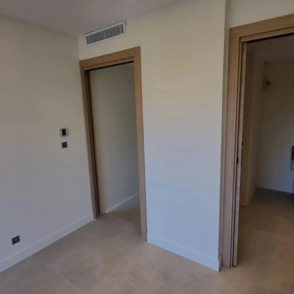 Couloir rénové avec deux portes à galandage encadrées de bois clair, grille de ventilation en hauteur et sol en grand carreau.