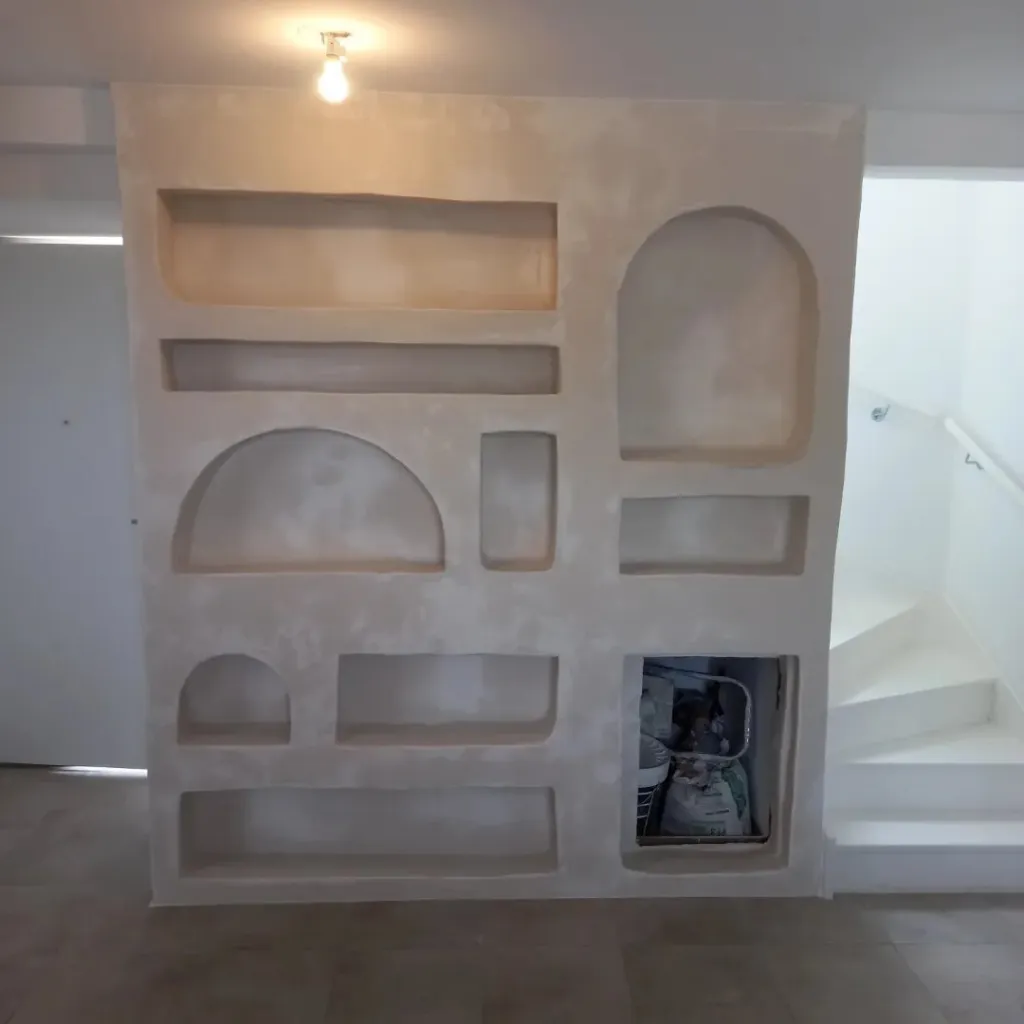 Vue de face d'un mur en plaque de plâtre avec étagères rectangulaires et arches décoratives, enduit mat non peint.