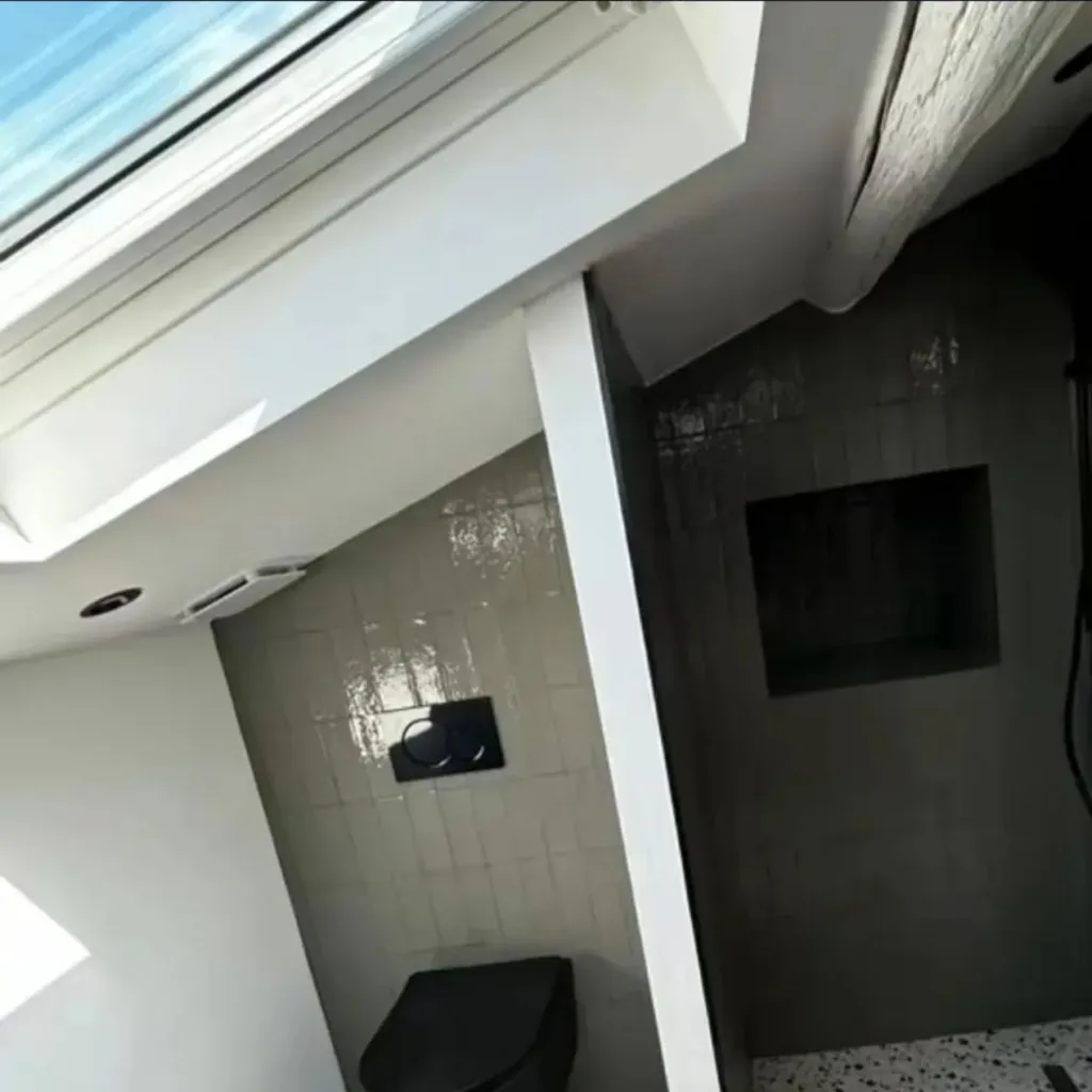 Salle d'eau sous combles avec douche carrelée vert, WC suspendu noir, receveur à caniveau et sol terrazzo.