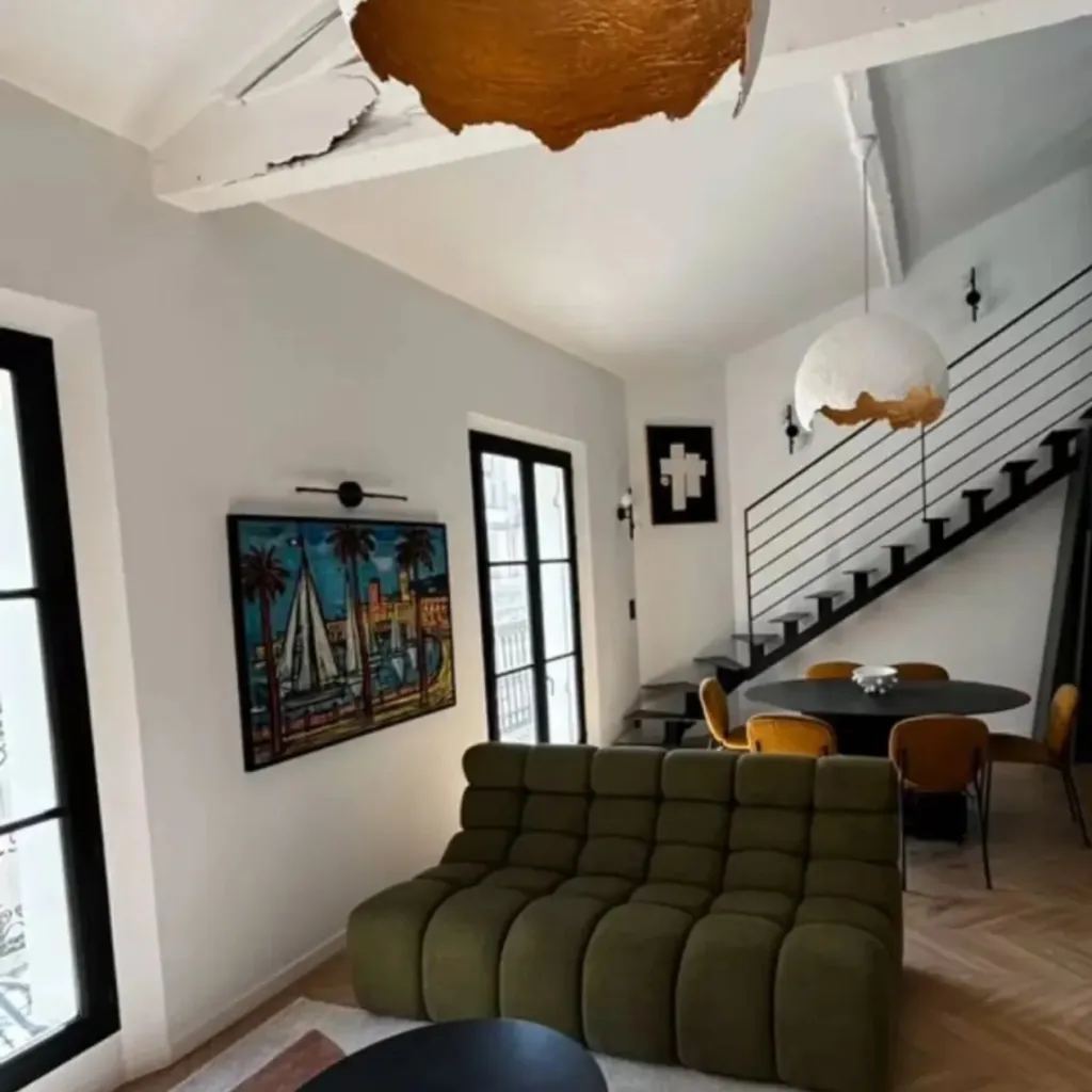 Séjour avec canapé vert, table ronde noire et escalier à limon central en acier menant à la mezzanine.