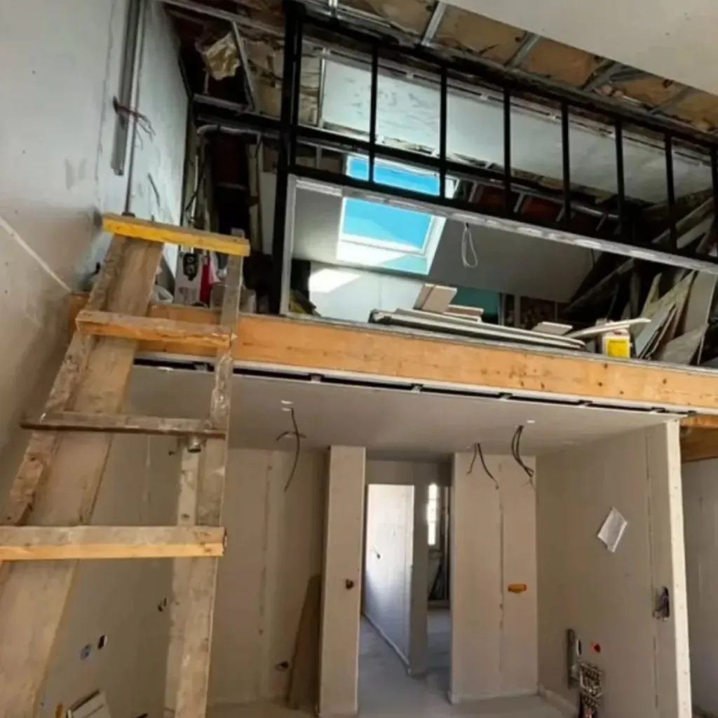 Intérieur en chantier avec mezzanine bois et acier sur cloisons de plaques de plâtre et échelle de chantier.