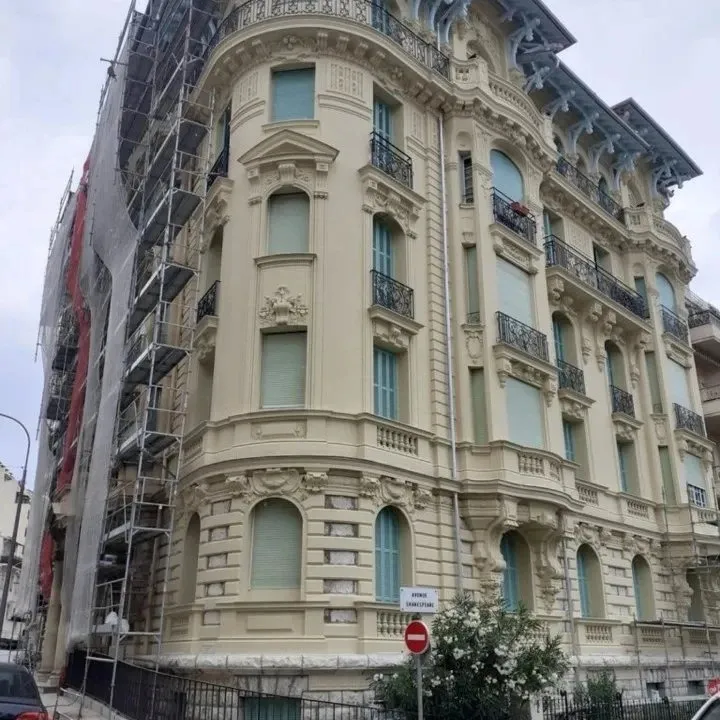 Angle arrondi d'un immeuble ancien aux ornements en pierre, échafaudé le long de la façade gauche.