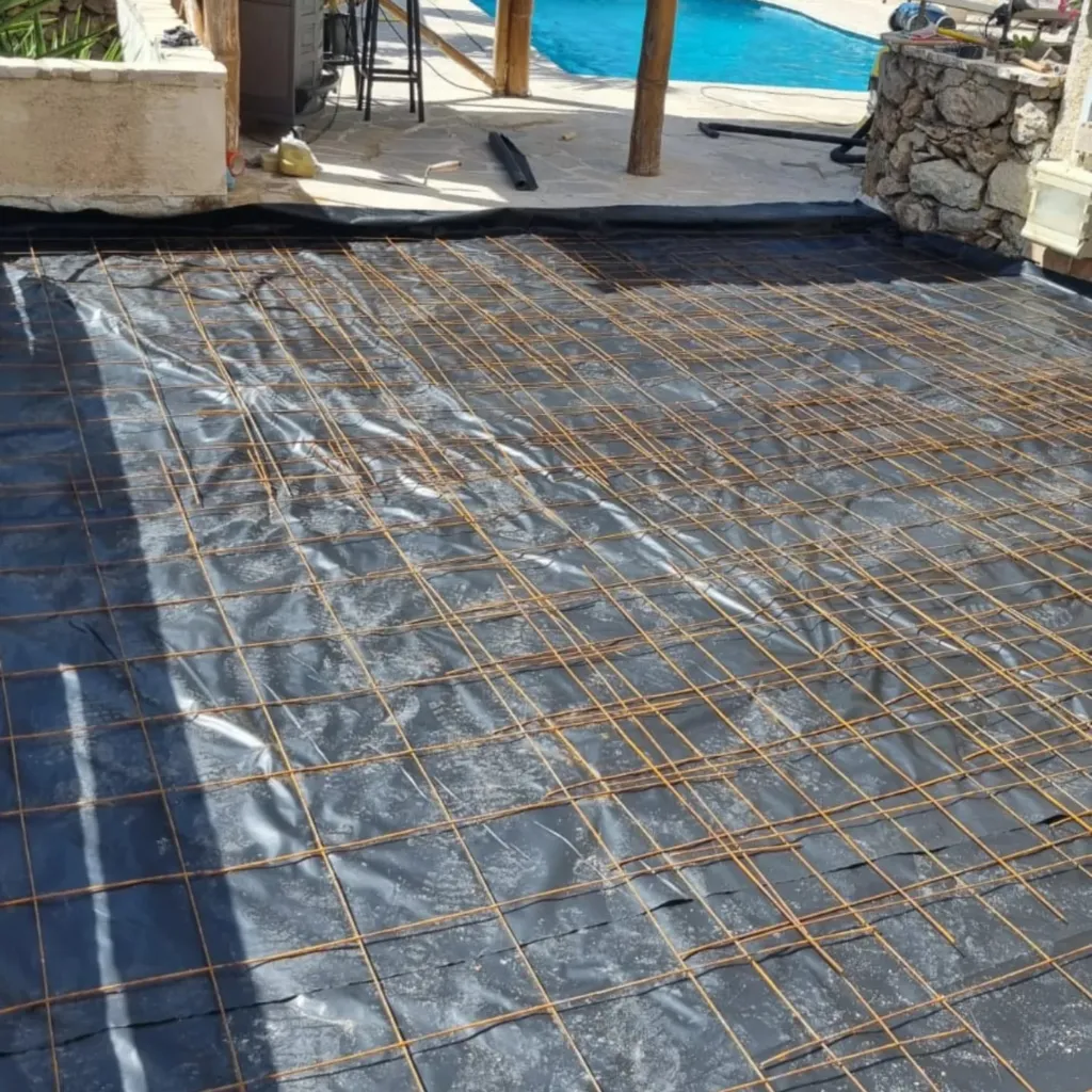 Treillis soudé posé sur un film polyane noir avant coulage de la dalle, piscine au fond.