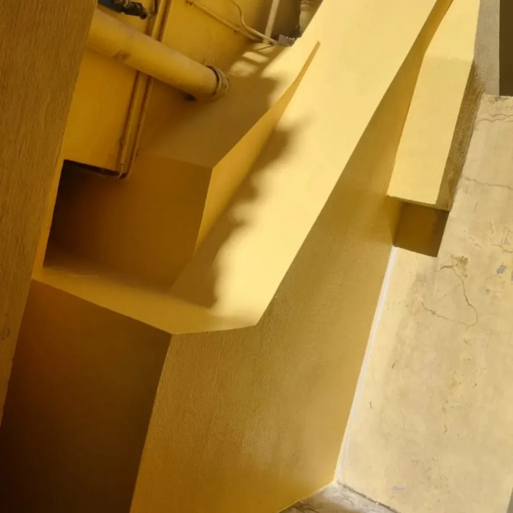 Angle de façade et conduit repeints d'un enduit jaune lisse après réparation.