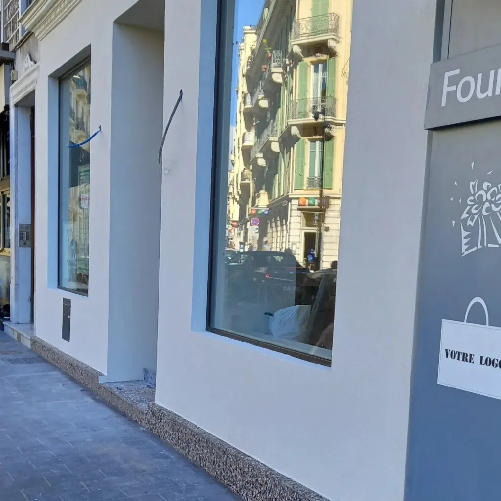 Devanture à enduit lisse clair, encadrements de vitrine et soubassement en granulats, trottoir pavé.