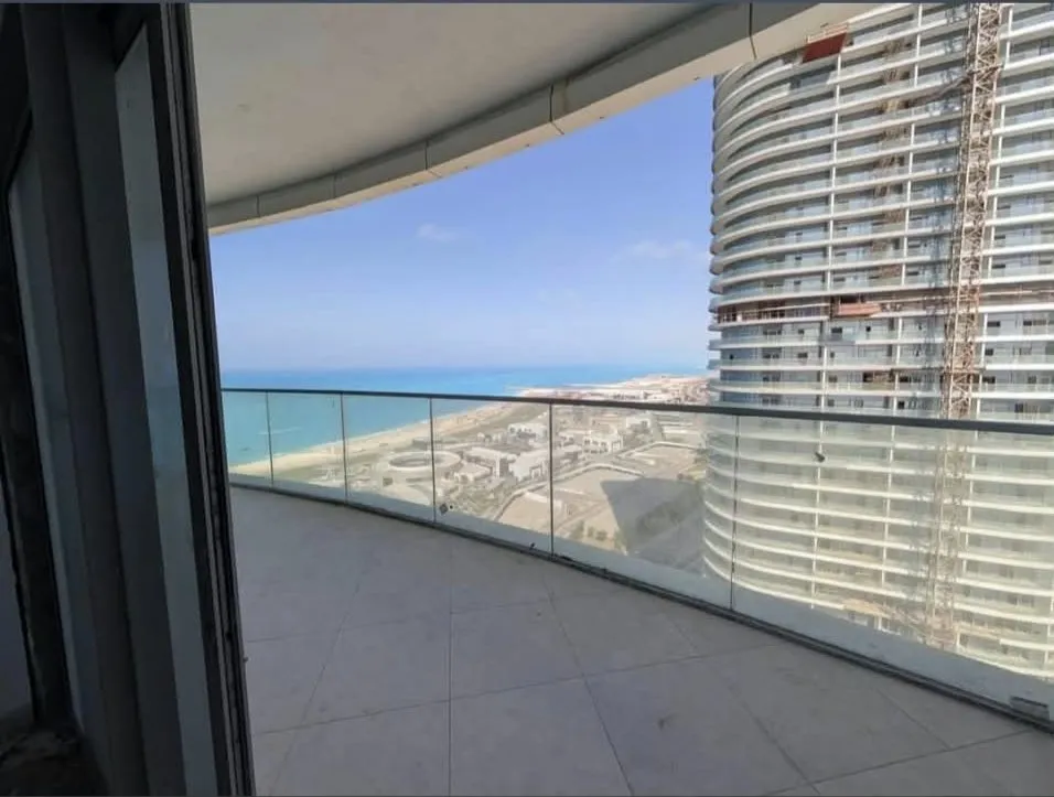 Balcon courbe avec garde-corps en verre, grand carrelage et vue sur la mer.