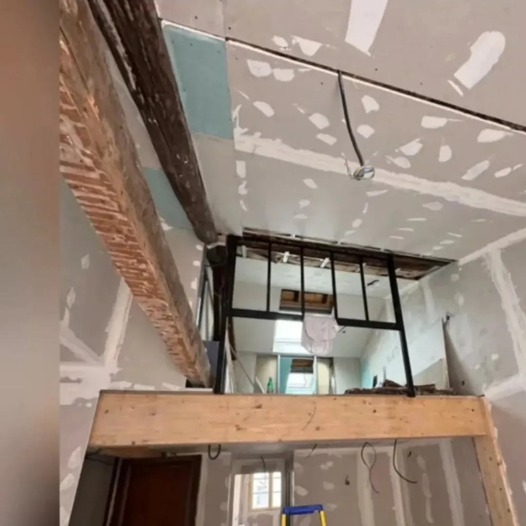 Plafond et murs en plaques de plâtre avec bandes à joints, poutre apparente et verrière métallique.