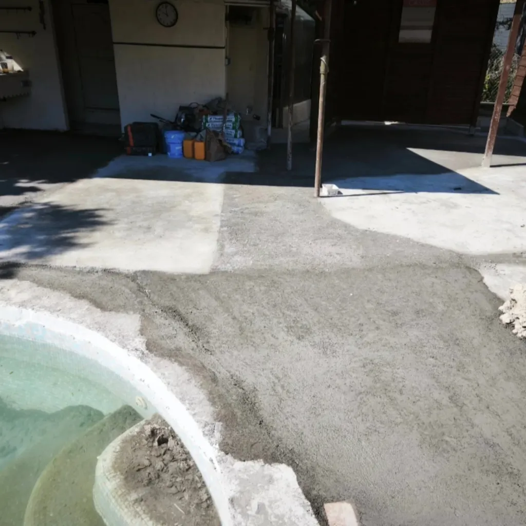 Chape fraîche étalée sur une plage de piscine en béton ancien, bassin au premier plan à gauche.