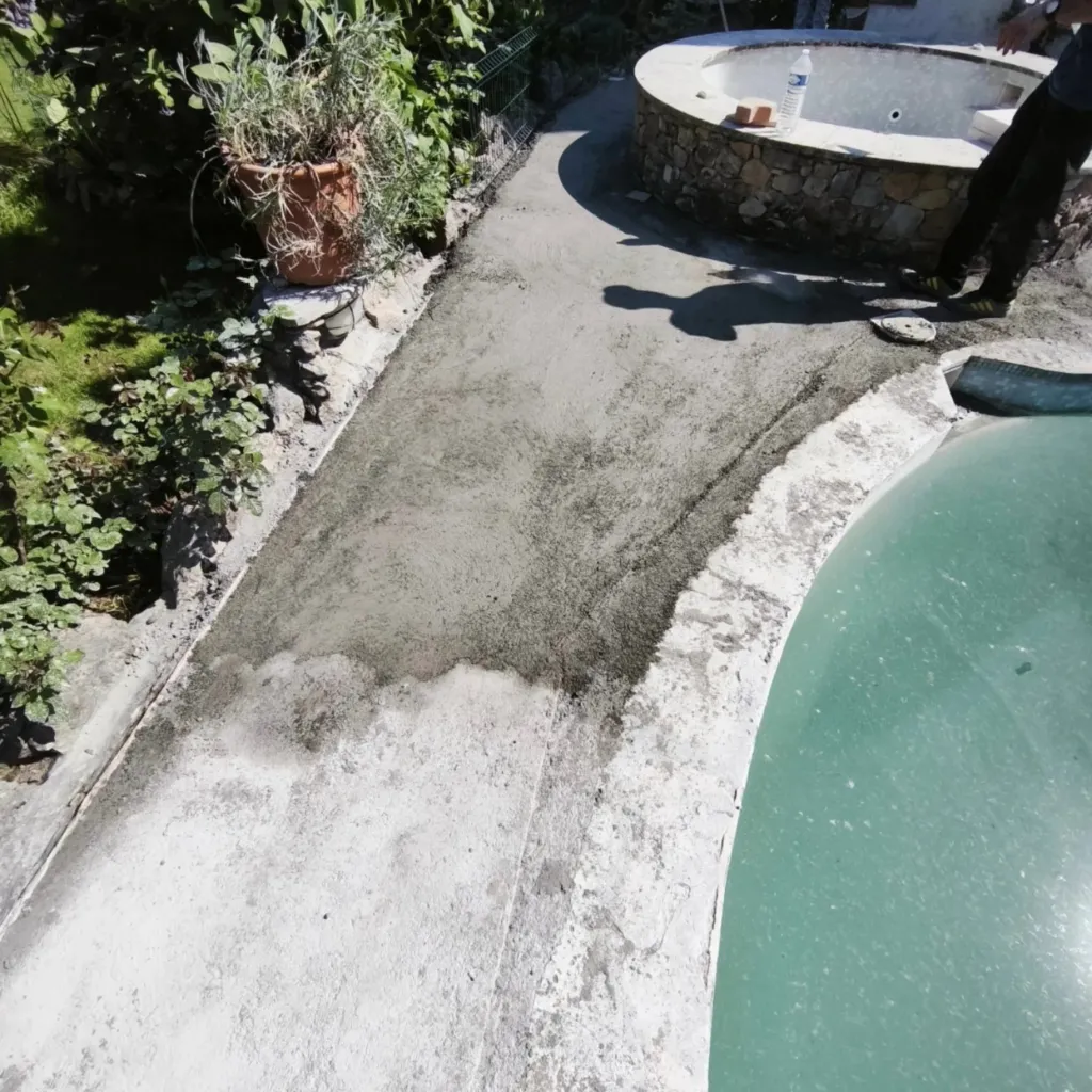 Chape grise étalée le long d'un bassin à bords arrondis, bordure de jardin et petite fontaine en pierre.