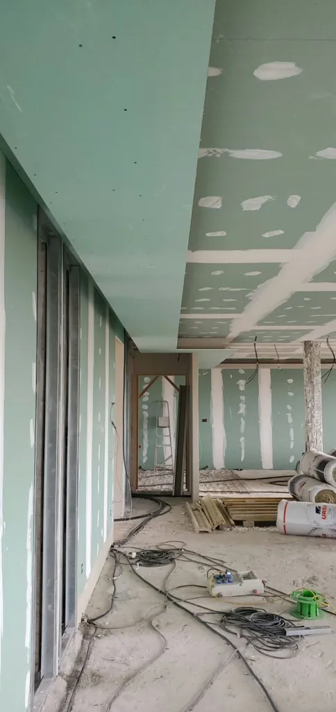 Plateau avec plafond et cloisons en plaques de plâtre vertes, joints bandés et câbles au sol.