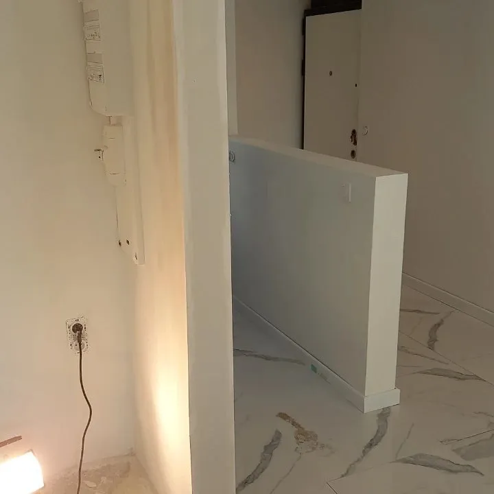 Angle de murs enduits et poncés avec plinthes blanches sur un sol en marbre, éclairage de chantier au sol.