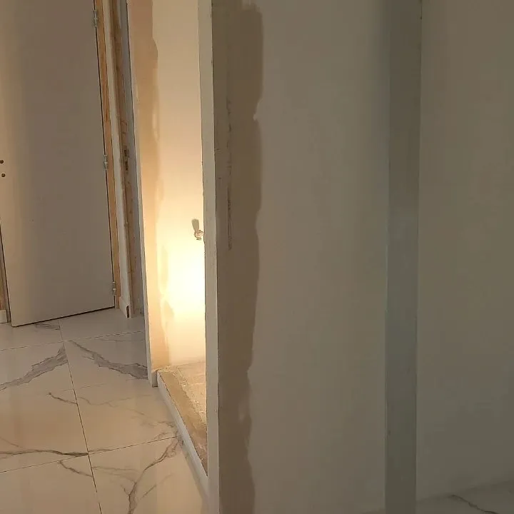 Pilier de plâtre avec reprise d'enduit partielle à côté d'une porte et d'un sol en marbre.