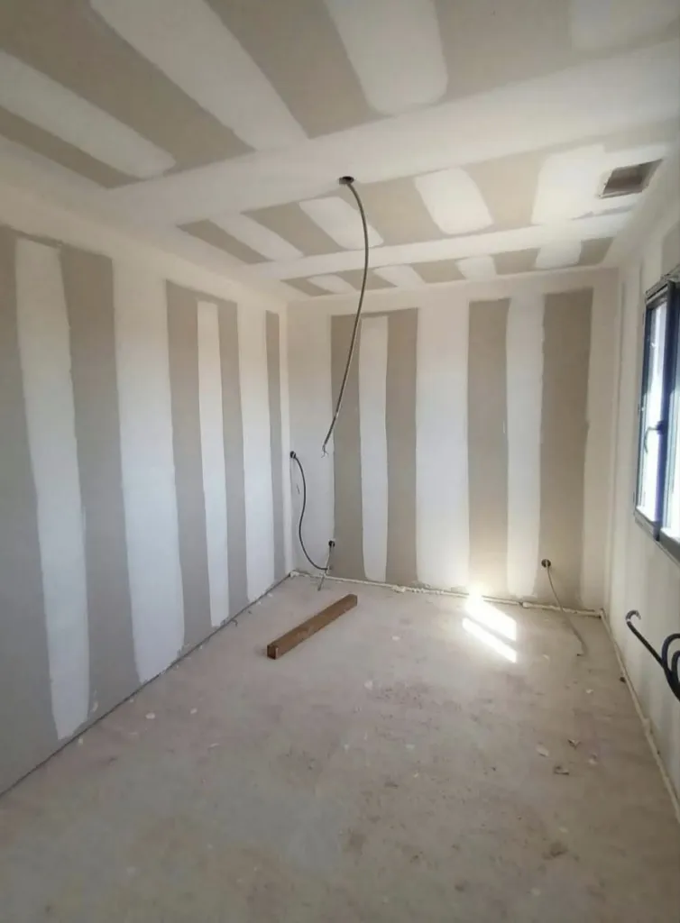 Pièce aux murs et plafond en plaques de plâtre avec bandes d'enduit apparentes, câbles au plafond.